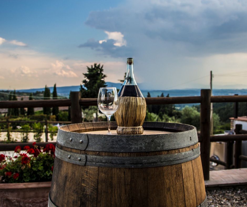 bouteille de Chianti et verre vide posés sur une barrique face à un paysage