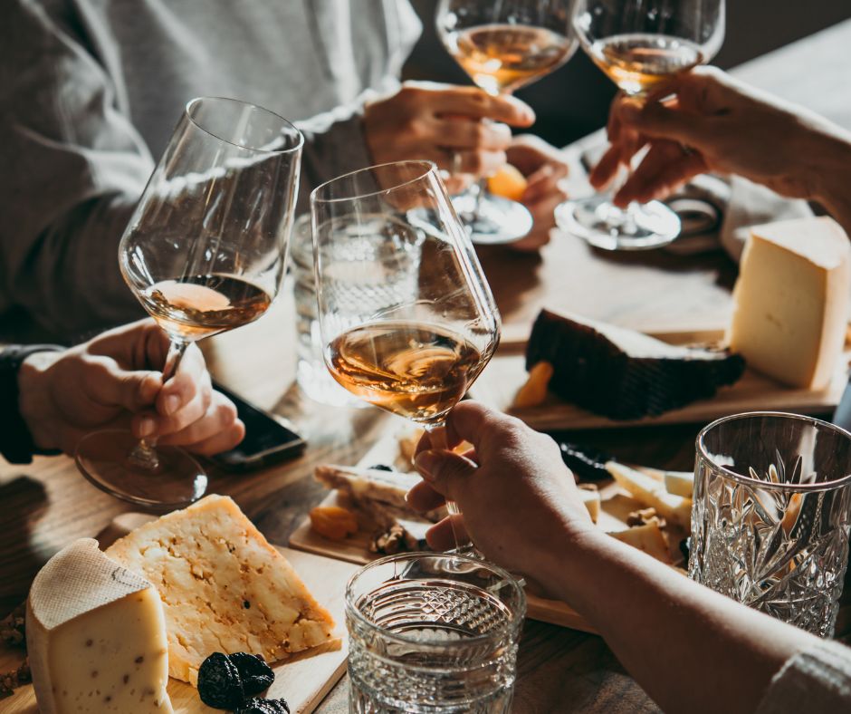 plateau de fromages sur une table et 4 verres de vins tenus pas 4 personnes en train de trinquer