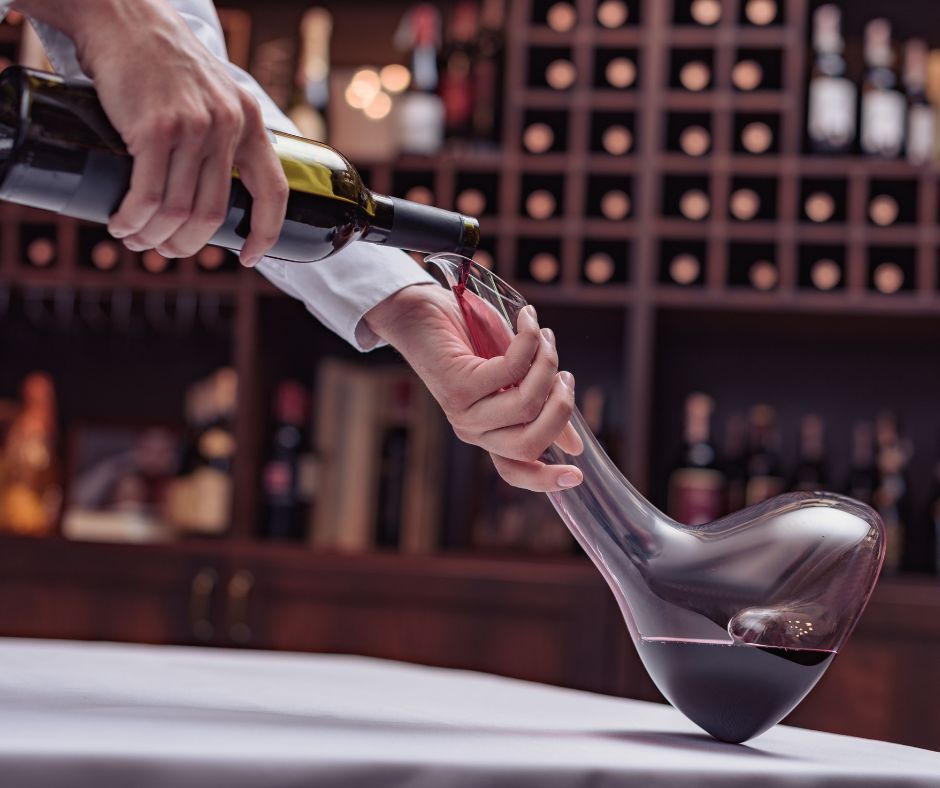 un sommelier vide une bouteille de vin rouge dans une carafe à décanter